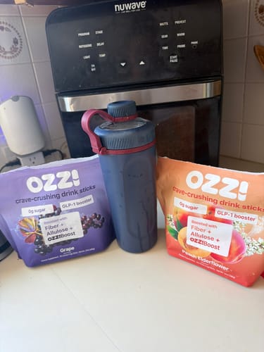 Customer's Ozzi Crave Crusher drink sticks in Grape and Peach Elderflower flavors on a counter with a shaker bottle.