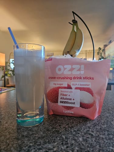 Reviewer's prepared OZZI! drink in a glass next to the pink crave-crushing drink sticks pouch.