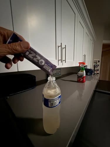 Customer pours a Grape Ozzi stick into a water bottle on the laundry-room counter.