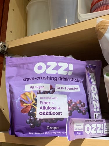 Reviewer's purple bag of Ozzi crave-crushing drink sticks in Grape flavor, shown on a shelf with two individual sticks.