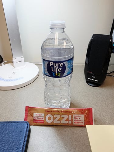 Customer's Ozzi crave-crushing drink stick on a desk next to a water bottle, ready to be mixed.