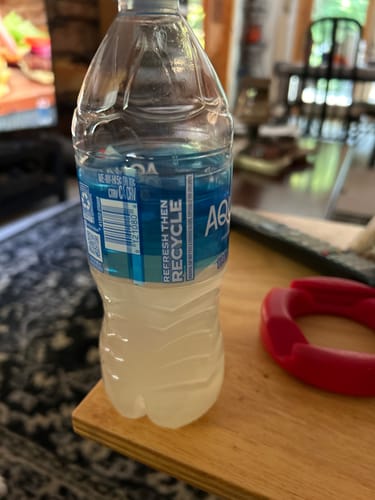 Customer's water bottle with The Crave Crusher v2 mixed in, creating a cloudy white liquid on a wooden table.