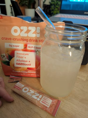 Reviewer's Peach Elderflower bag and stick of Ozzi next to a prepared mason-jar drink with a glass straw.