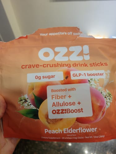 Customer holds up a Peach Elderflower bag of Ozzi crave-crushing drink sticks.