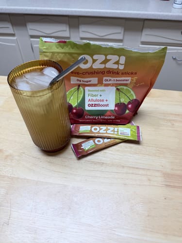 Customer's Ozzi Cherry Limeade drink mix bag and packets with a prepared drink in a glass on a wooden counter.