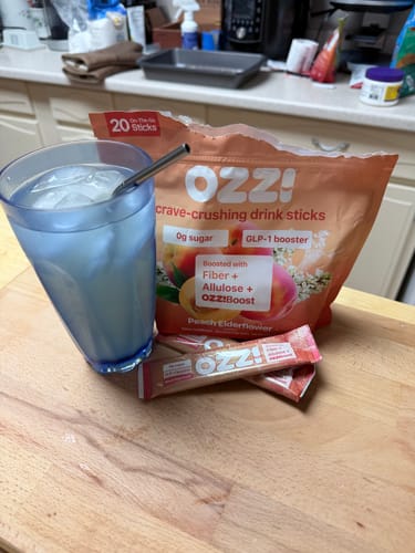 Reviewer's bag of Ozzi crave-crushing drink sticks with two packets and a prepared drink in a glass on a counter.