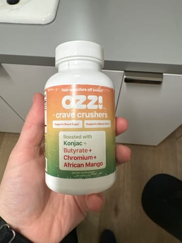 Reviewer holds a bottle of Ozzi Crave Crushers capsules in their kitchen.